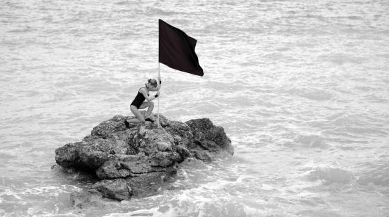 Kvinne planter et svart flagg i strandkanten.