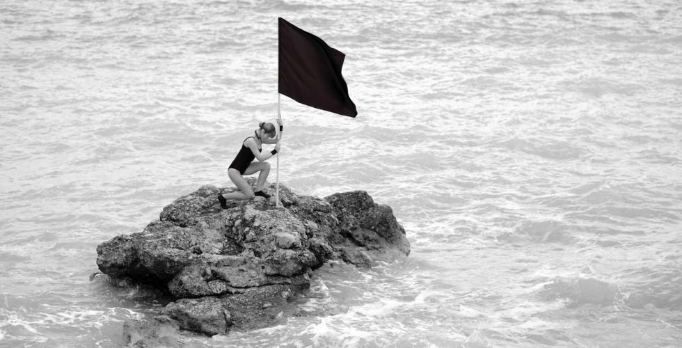 Kvinne planter et svart flagg i strandkanten.
