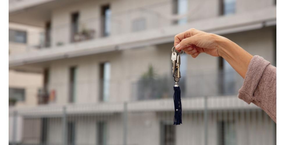 Hånd holder nøkkelknippe foran leilighetsbygg.