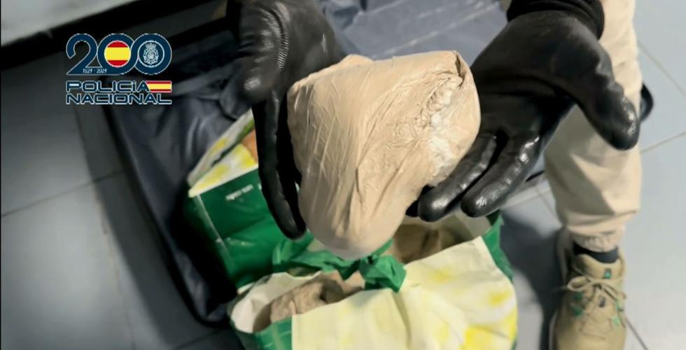 Politibetjent holder en brun pakke foran en koffert. 
